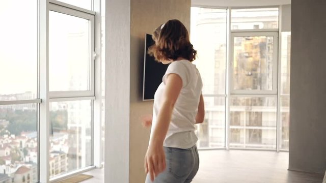 Happy woman in headphones listening music while having fun and dancing on kitchen