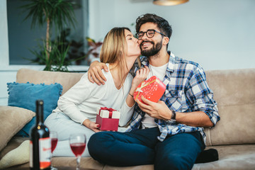 Man surprising his girlfriend with a gift on the couch at home in the living room