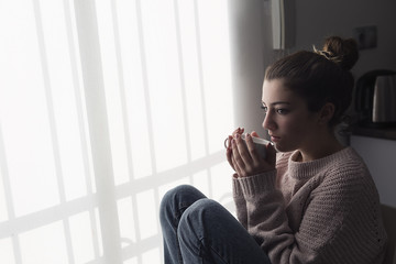 Teen girl sitting by a window with a cup of coffee in her hand.