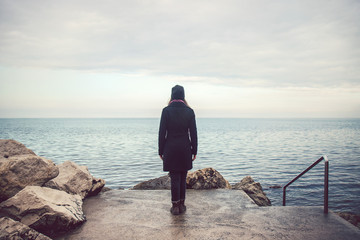 lonely sad woman looking the horizon, solitude concept in sea landscape with gray cloud (winter...