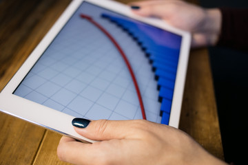 The girl working with a tablet computer. The graph rises. Table, wooden, background black.