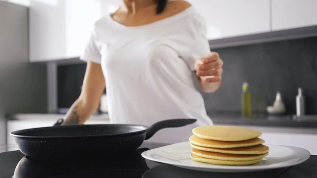 Cropped image of a smiling asian woman standing by the stove on kitchen and cooking pancakes

