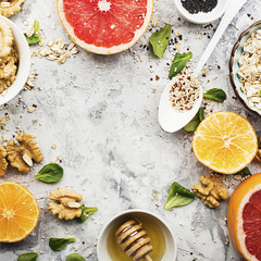 Ingredients of healthy breakfast food: oat flakes, kinoa, walnuts, floral honey, greens, oranges, bloody grapefruits on a light marble background. Top View.