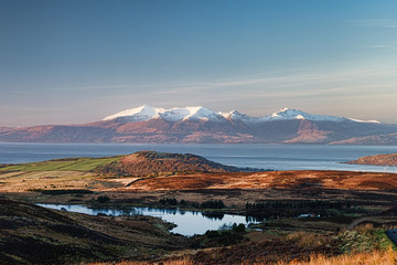 A rugged Scottish hillside in winter after the snow had melted. A broken down stone wall or dyke covered in moss and stone dykes running up the hillside.