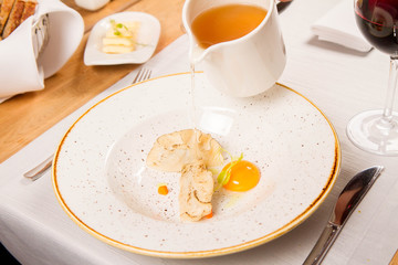 Broth with dumplings and an egg yolk being poured from a jug