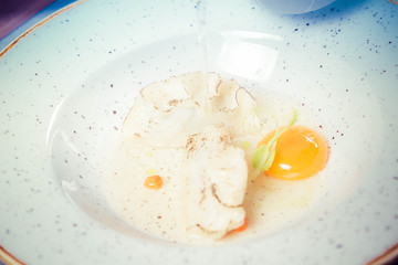 Broth with dumplings and an egg yolk being poured from a jug