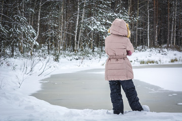 Child down on the frozen lake in winter forest