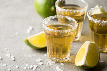 Macro focus photo of shots of golden Mexican tequila with lime and salt on wooden background. Alcoholic drink concept.
