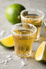 Macro focus photo of shots of golden Mexican tequila with lime and salt on wooden background. Alcoholic drink concept.