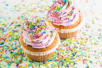 Closeup of cupcakes with vanilla, berries, pink and white cream, chocolate and sprinkles on wooden background. Selective focus. Sweet dessert tasty food concept muffin.