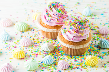 Closeup of cupcakes with vanilla, berries, pink and white cream, chocolate and sprinkles on wooden background. Selective focus. Sweet dessert tasty food concept muffin.