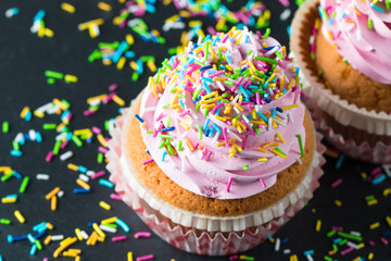 Closeup of cupcakes with vanilla, berries, pink and white cream, chocolate and sprinkles on wooden background. Selective focus. Sweet dessert tasty food concept muffin.