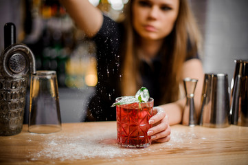 pretty barista finishes preparation of pink alcoholic cocktail by adding a bitter of powdered sugar
