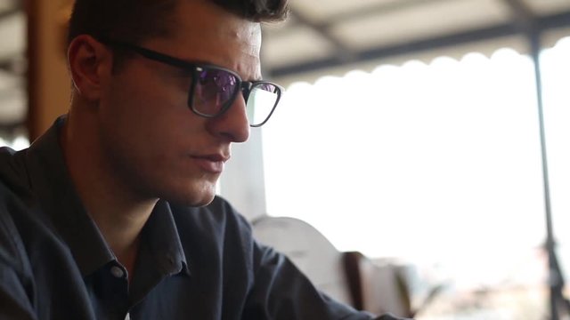Camera slides from freelancer's hands typing on laptop keyboard to the handsome businessman in glasses working on computer in cafe. Revealing shot. Business concept