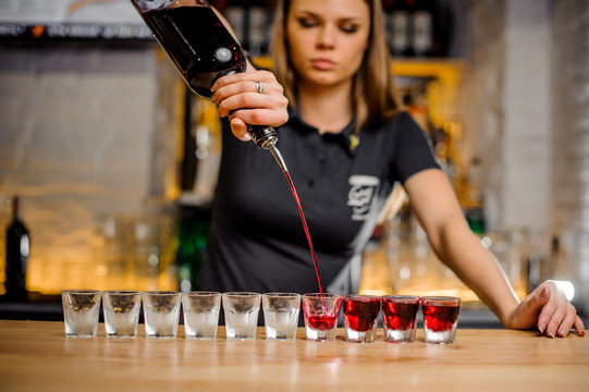 professional barmaid pours alcohol into stacks that are lined up