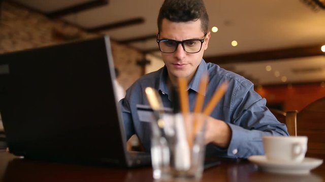 Young man shopping on the internet and paying with credit card. Handsome freelancer businessman in glasses replenish his stock exchange account with laptop via web application. Business concept.