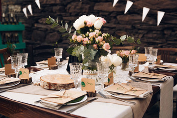 Little dinner table served in rustic style and decorated with pink flowers stands outside