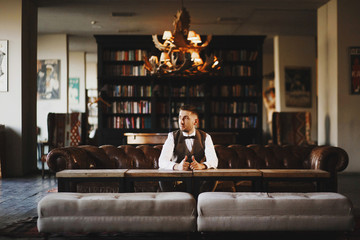 Thoughtful man in grey waistcoat poses in the dark library