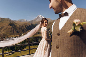 Groom in modern suit and bride in charming pink dress pose on the terasse with great mountain view...