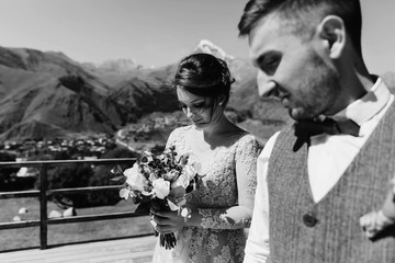 Groom in modern suit and bride in charming pink dress pose on the terasse with great mountain view...