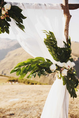 Wedding altar made of wooden blocks, greenery, roses and white cloth stands on the top of the...