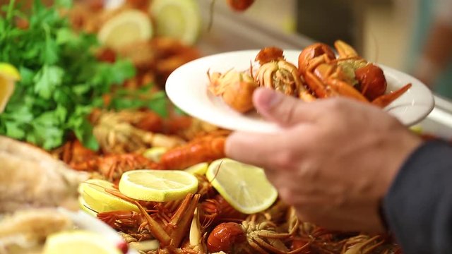 Closeup view of boiled red crayfish on tray on table at restaurant. Man puts some on his plate.
