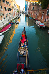 Fototapeta na wymiar Venetian gondolier punting gondola through green canal waters of Venice, Italy