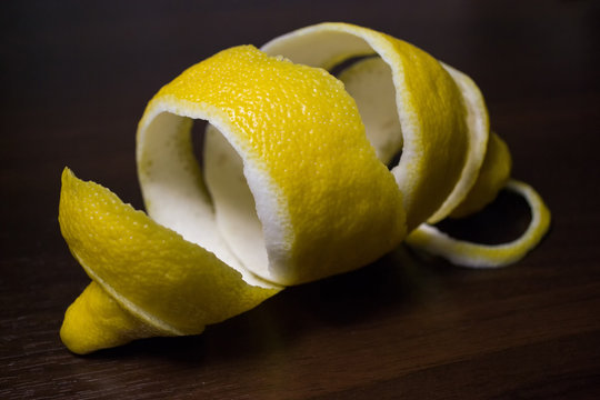 Lemon peel or lemon twist on a dark brown wooden background. Lemon slices are cut across. Close up Cítrus límon.