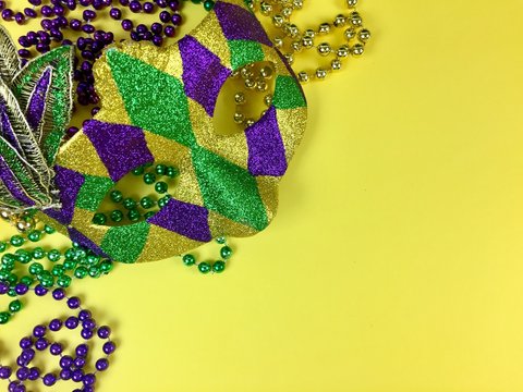Mardi Gras mask and beads on a yellow background