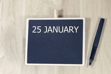 sentence JAN 25 written with chalkboard on a wooden table with pen.