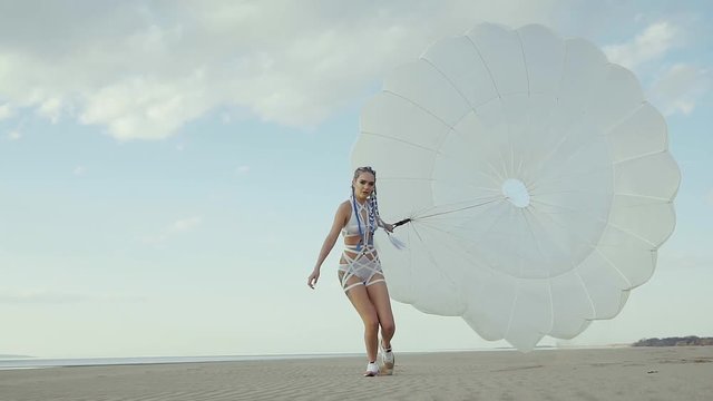 Eccentric freedom-loving girl is wearing strange swimsuit is walking over seacoast with large white canopy. It is swaying by wind of summer day.