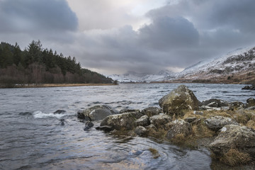 Beautiful Winter landscape image of Llynnau Mymbyr in Snowdonia National Park with snow capped mountains in background
