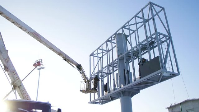 Builder on a Lift Platform at a construction site. Men at work. construction worker assembling scaffold on building site. Men assemble Billboard on tap