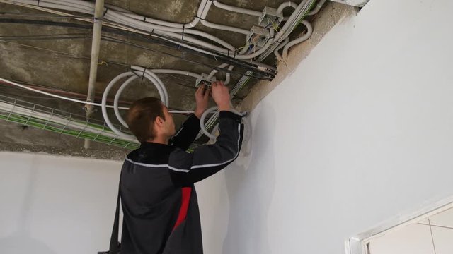 Man working with wires in the ceiling. Installing a spotlight in the room. A man is using an insulating tape to the bare electric wires