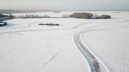 Fototapeta na wymiar One car driving through the winter forest on country road. Top view from drone. Aerial view of snow covered road in winter, car passing by. Top view of the car traveling on snowy road