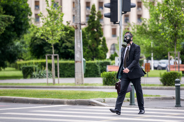 Businessman cross the street outdoor with briefcase wearing a gas mask on the face.