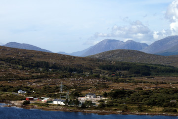 A very busy landscape with water, buildings, pylons, trees and mountains