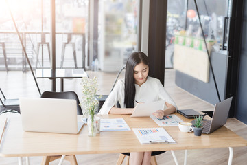 Asian beautiful young business woman in white shirt smiling working on desk with laptop and financial report document.