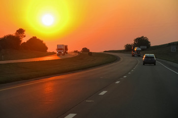 Highway with trucks and cars on the background of the setting sun