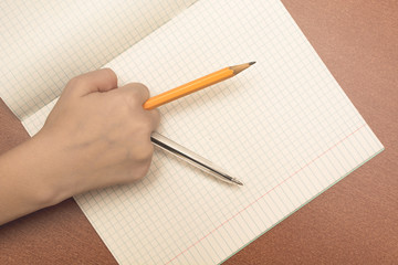 The hand of a schoolgirl holding pencil and pen