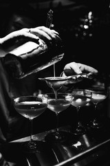 black and white close photograph bartender hands, which makes and pours cocktail from shaker into glass - 187984842