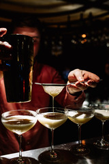 close up bartender hands, which makes and pours cocktail from shaker into glass