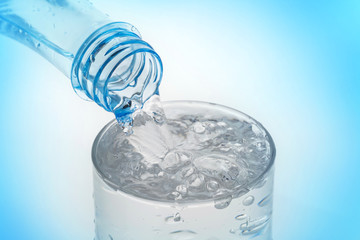 Pouring water from bottle into glass on blue background.