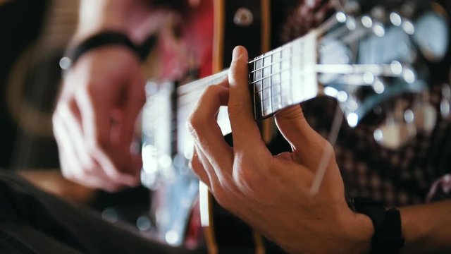 Male musician plays the guitar, hands close up, focus on the guitar fretboard