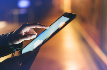 Girl holding in hands on blank clean screen tablet on background glow bokeh lights in night atmospheric city, hipster hands using template mobile computer on lights car glitter street; mockup gadget