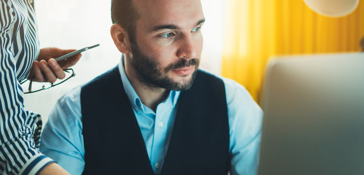 Bearded young businessman working on modern office at night. Consultant man thinking looking in monitor computer. Manager typing on keyboard in coworking workplace, startup project concept in studio