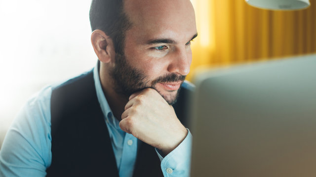 Bearded young businessman working on modern office at night. Consultant man thinking looking in monitor computer. Manager typing on keyboard in coworking workplace, startup project concept in studio