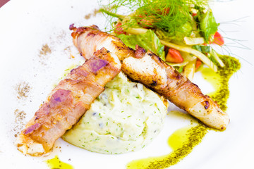 Pike perch wrapped in bacon, mashed potatoes and vegetable salad on white plate