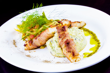 Pike perch wrapped in bacon, mashed potatoes and vegetable salad on white plate