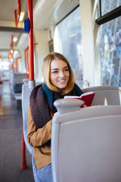 Young happy woman sitting in city bus and reading book